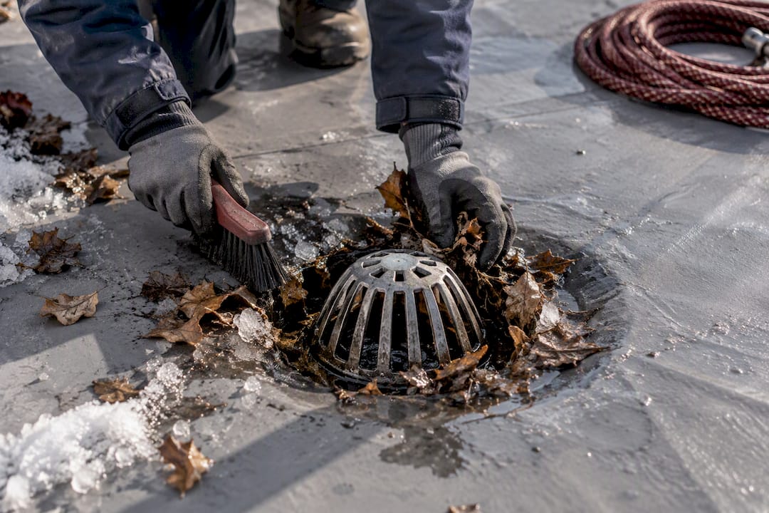 Worker clearing debris from commercial roof drain